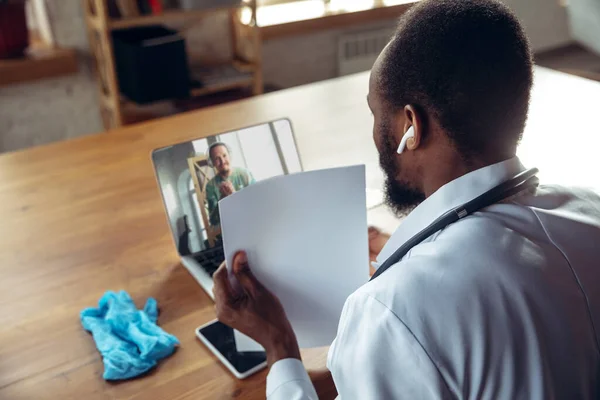 Doctor advising the patient online with laptop. African-american doctor during his videocall, work with patients, explaining recipes for drug.