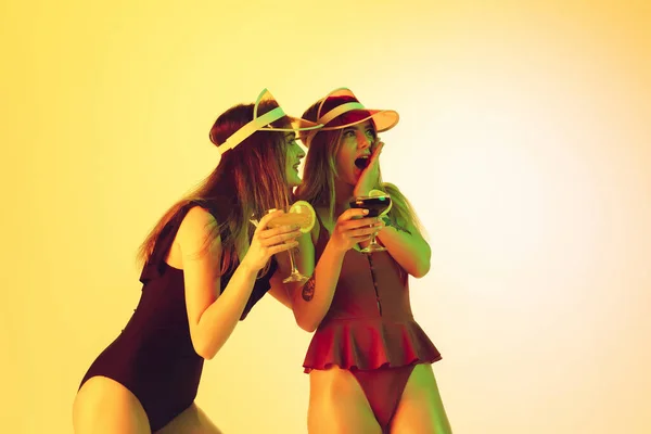 Красиві дівчата в модних купальниках ізольовані на жовтому студійному фоні в неоновому світлі. Літо, курорт, мода та концепція вихідних. Пивні коктейлі . — стокове фото