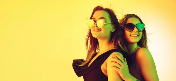 Cerca de hermosas chicas en trajes de baño de moda y gafas aisladas en el fondo del estudio amarillo en luz de neón. Verano, resort, moda y concepto de fin de semana. Folleto con copyspace . —  Fotos de Stock