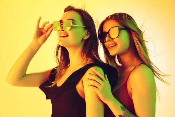 Zamknij piękne dziewczyny w modne stroje kąpielowe i okulary izolowane na żółtym tle studio w neonowym świetle. Koncepcja lata, kurortu, mody i weekendu. — Zdjęcie stockowe
