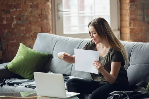 Молодая женщина, деловая женщина работает или учится дома, смотрит на экран компьютера, монитор, держит белый лист, доску. Акцентирован, сконцентрирован. Авторское пространство. Вид сверху . — стоковое фото