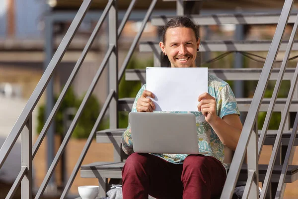 Joven, hombre de negocios trabajando al aire libre, mirando en la pantalla de la computadora, monitor, la celebración de la hoja blanca en blanco, pizarra blanca. Espacio de copia . — Foto de Stock
