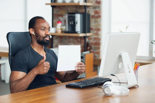Joven, hombre de negocios trabajando en la oficina, mirando en la pantalla de la computadora negra en blanco, monitor, sosteniendo la hoja blanca en blanco, pizarra blanca. Espacio de copia . — Foto de Stock