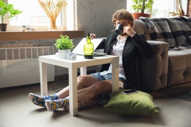 Pantolonsuz ama ceketli genç bir adam bilgisayar ve dizüstü bilgisayarla çalışıyor. Coronavirus sırasında uzak ofis, iç çamaşırlarıyla eğlenceli ve rahat bir iş.