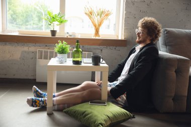 Pantolonsuz ama ceketli genç bir adam bilgisayar ve dizüstü bilgisayarla çalışıyor. Coronavirus sırasında uzak ofis, iç çamaşırlarıyla eğlenceli ve rahat bir iş.