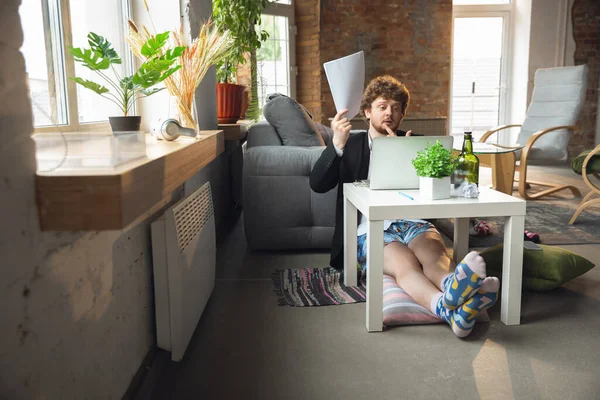 Young man without pants but in jacket working on a computer, laptop. Remote office during coronavirus, fun and comfortable work in underpants — Stock Photo, Image