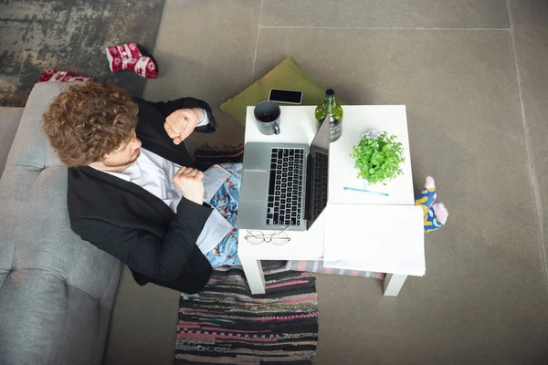 Молодой человек без штанов, но в куртке, работает за компьютером, ноутбуком. Удаленный офис во время коронавируса, веселая и удобная работа в трусах — стоковое фото