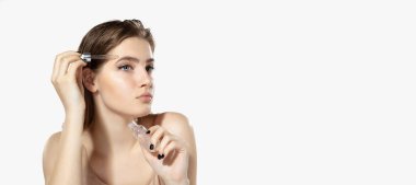 Gençlik sırları. Serumlu, beyaz arka planda gerekli yağı olan genç ve güzel bir kadına yakın durun. Kozmetik ve makyaj, doğal ve eko tedavi, cilt bakımı.