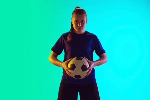 Vrouwelijk voetbal, football speler die bal vasthoudt, zelfverzekerd poserend geïsoleerd op een hellende achtergrond. Kopieerruimte. — Stockfoto