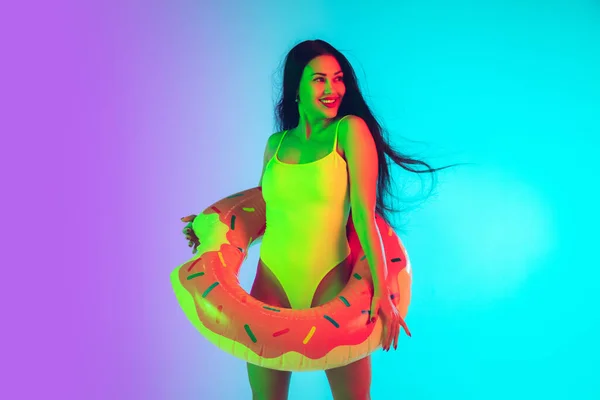 Beautiful girl in fashionable swimsuit isolated on gradient studio background in neon light. Summer, resort, fashion and weekend concept — Stock Photo, Image