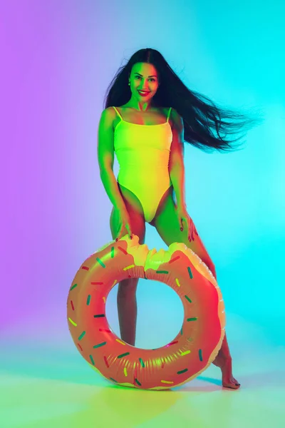 Beautiful girl in fashionable swimsuit isolated on gradient studio background in neon light. Summer, resort, fashion and weekend concept — Stock Photo, Image