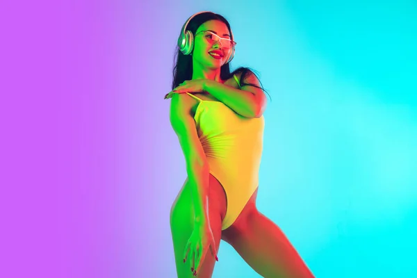 Hermosa chica en traje de baño de moda aislado en el fondo del estudio gradiente en luz de neón. Verano, resort, moda y concepto de fin de semana —  Fotos de Stock