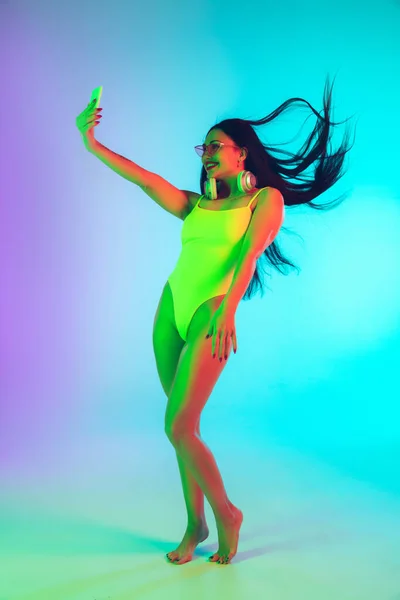 Menina bonita em maiô elegante isolado no fundo do estúdio gradiente em luz de néon. Verão, resort, moda e conceito de fim de semana — Fotografia de Stock