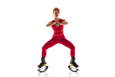 Kırmızı spor kıyafetli güzel bir kadın kangoya atlıyor beyaz stüdyo arka planında izole edilmiş ayakkabılar giyiyor..