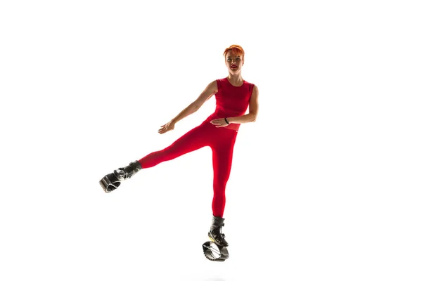 Beautiful redhead woman in a red sportswear jumping in a kangoo jumps shoes isolated on white studio background. — Stock Photo, Image