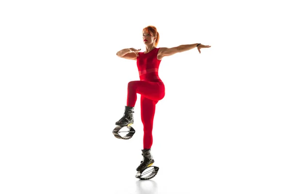 빨간 운동복을 입은 아름다운 빨간 머리 여자가 흰색 스튜디오 배경에 고립된 칸고오 신발을 신고 점프하는 모습. — 스톡 사진
