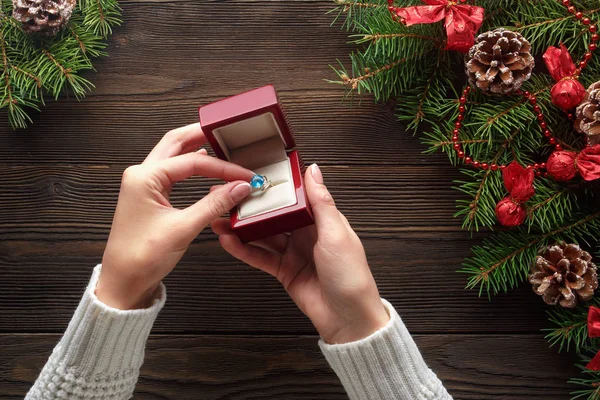 Anillo de compromiso en manos femeninas entre decoraciones navideñas sobre fondo de madera — Foto de Stock