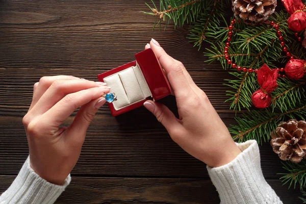 Anillo de compromiso en manos femeninas entre decoraciones navideñas sobre fondo de madera —  Fotos de Stock