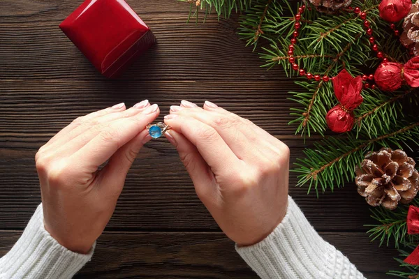 Anillo de compromiso en manos femeninas entre decoraciones navideñas sobre fondo de madera — Foto de Stock