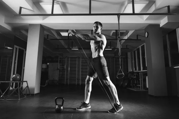 与拉伸弹性橡皮筋在健身房锻炼的健美男子 — 图库照片