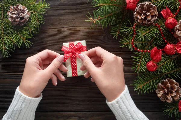 Vackra kvinnliga händer som håller en julklapp i låda med röd rosett. — Stockfoto