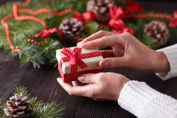 Vackra kvinnliga händer som håller en julklapp i låda med röd rosett. — Stockfoto