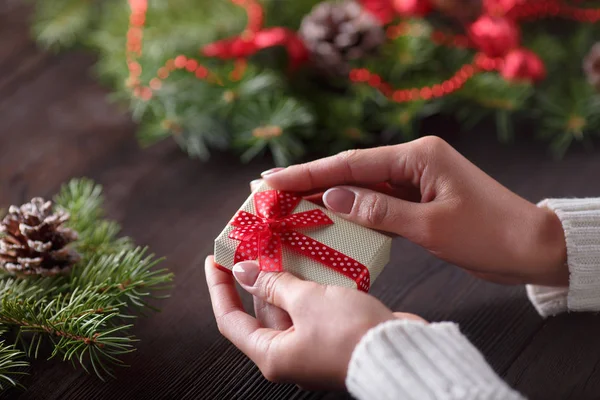 Vackra kvinnliga händer som håller en julklapp i låda med röd rosett. — Stockfoto