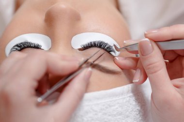 Stylist lengthening lashes for female in a beauty salon. clipart