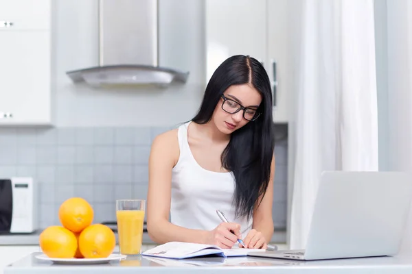 Mädchen mit Brille schreibt Hausaufgabe in Küche. — Stockfoto