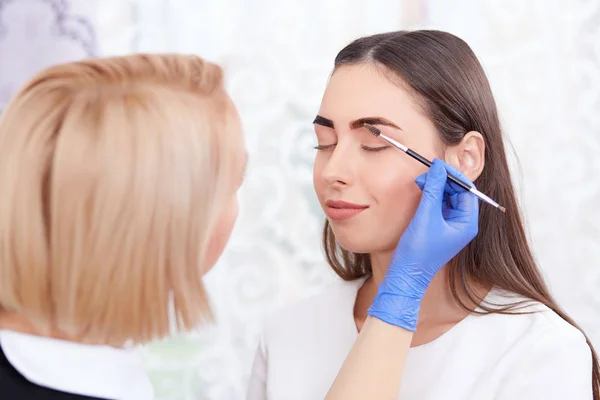 Cosmetologist em luvas que fazem sobrancelhas permanentes para a mulher . — Fotografia de Stock