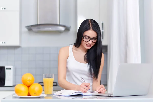 Girl in glasses writing home task at kitchen. — Stock Photo, Image