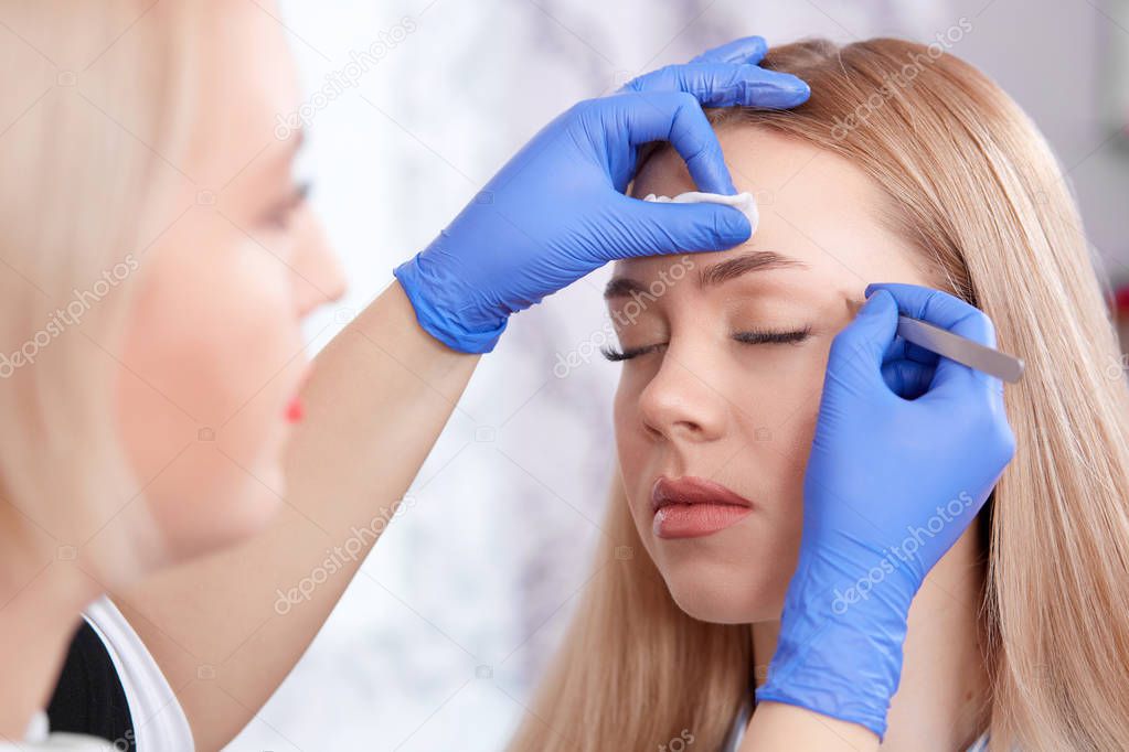 Cosmetologist in gloves plucking eyebrows fol woman.