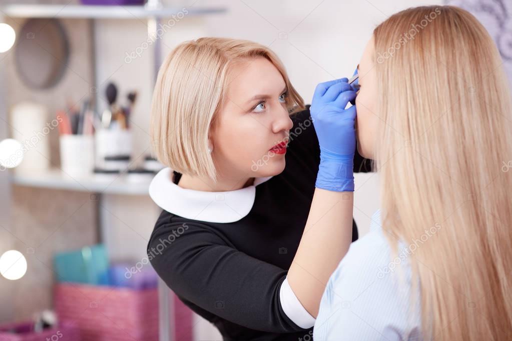 Cosmetologist plucking eyebrows for blonde woman.