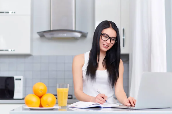 Brunette girl planing day at kitchen and using laptop. — Stock Photo, Image