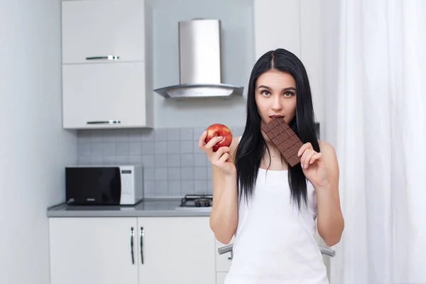 Attractive brunette eating chocolate and posing at camera. — Stock Photo, Image