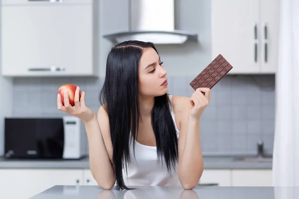 Mujer eligiendo comida chatarra o saludable, sosteniendo manzana y chocolate . — Foto de Stock