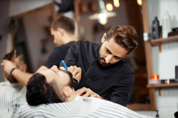 Концентрированный парикмахер бреется молодой человек — стоковое фото