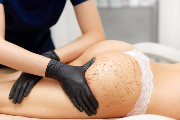 Manos de masajista y nalgas de cliente teniendo masaje exfoliante . — Foto de Stock