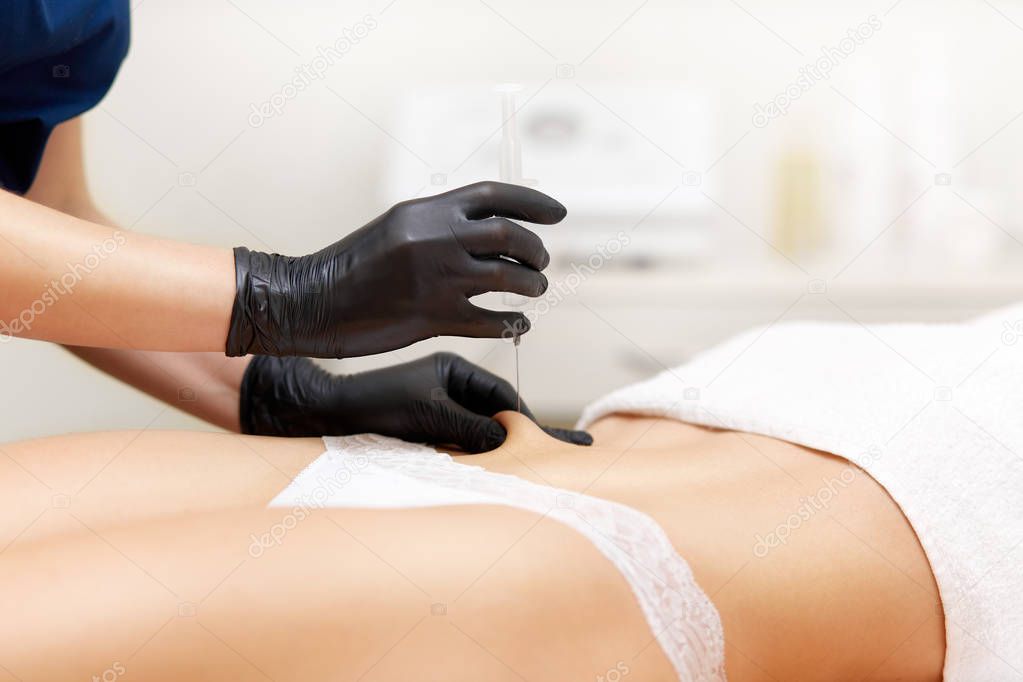 Cosmetologist doing lifting and correcting injection in belly.
