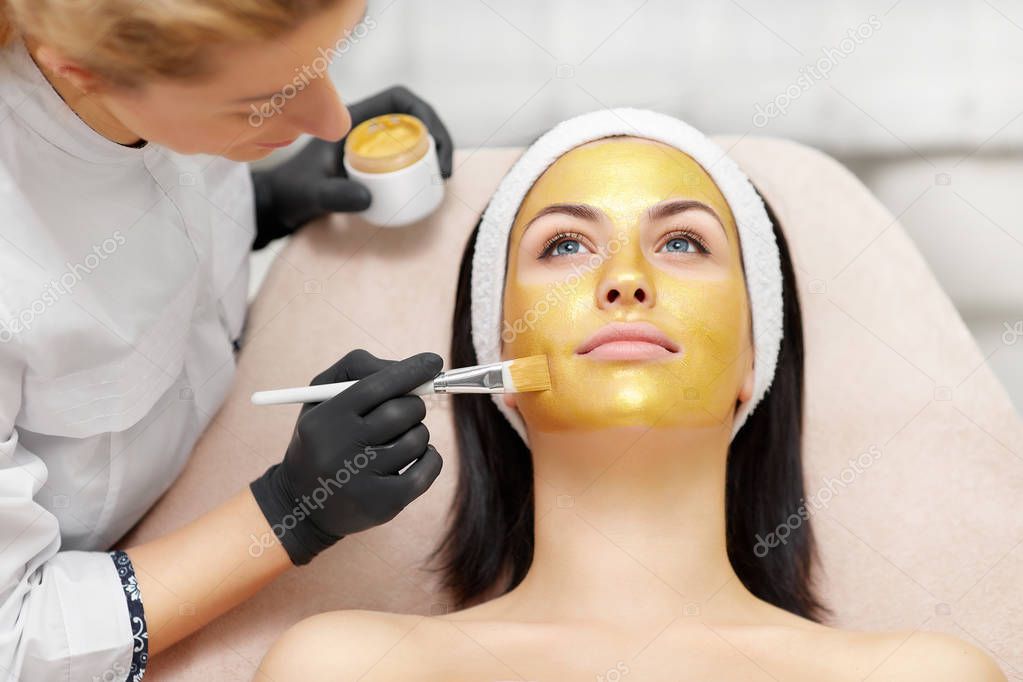 Applying of gold facial mask on skin of beautiful brunette.