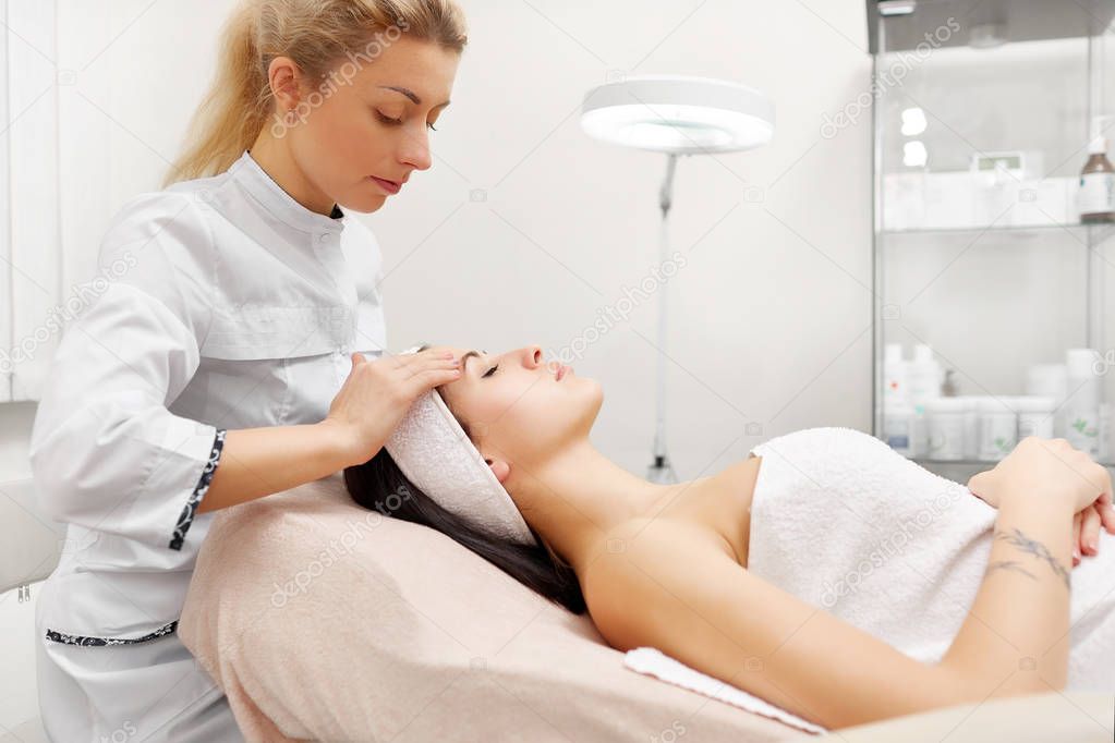 Beautiful woman having her face massaging and moisturizing in beauty salon.