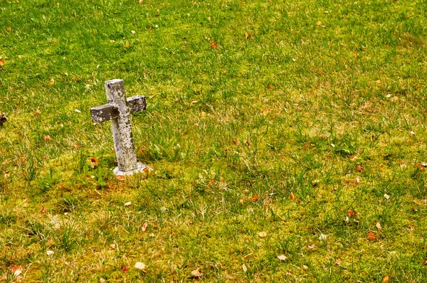 Pequeña cruz de piedra en la hierba . — Foto de Stock