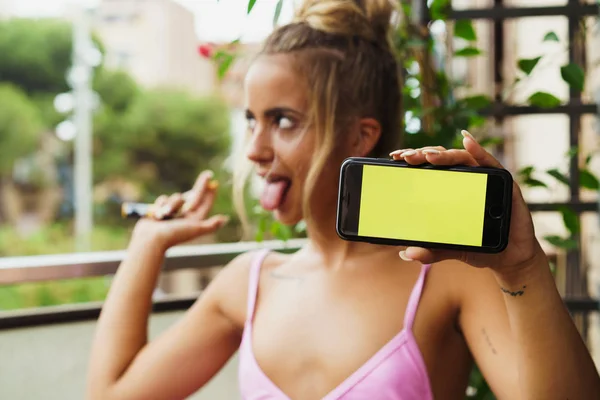 Hravá žena ukazuje smartphone při kouření — Stock fotografie