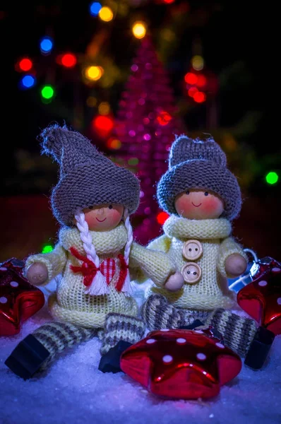 Dolls of a boy and a girl sitting on the snow with stars on the background of festive lights — Stock Photo, Image