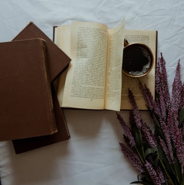 Açık kitabın üzerinde bir fincan kahve duruyor. Yakınlarda yıpranmış kapaklar ve lavanta dalları olan kitaplar var. Retro fotoğraf. Vintage fotoğraf.