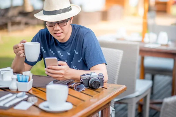 Fiatal ázsiai férfi intelligens telefon használata során reggelizik — Stock Fotó