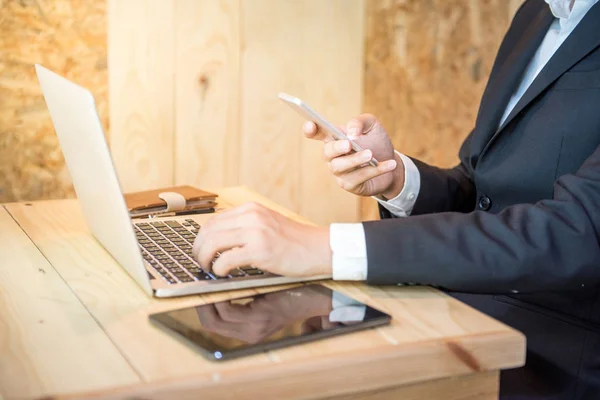 Homem de negócios segurando smartphone e usando laptop — Fotografia de Stock