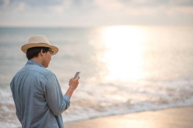 Genç adam sahilde akıllı telefon tutuyor.