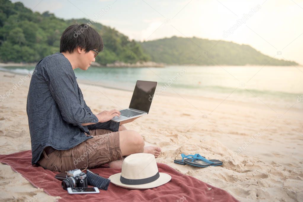 Young Asian man working with laptop on the beach