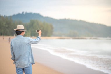 genç adam akıllı telefon tarafından sahilde fotoğraf çekmek